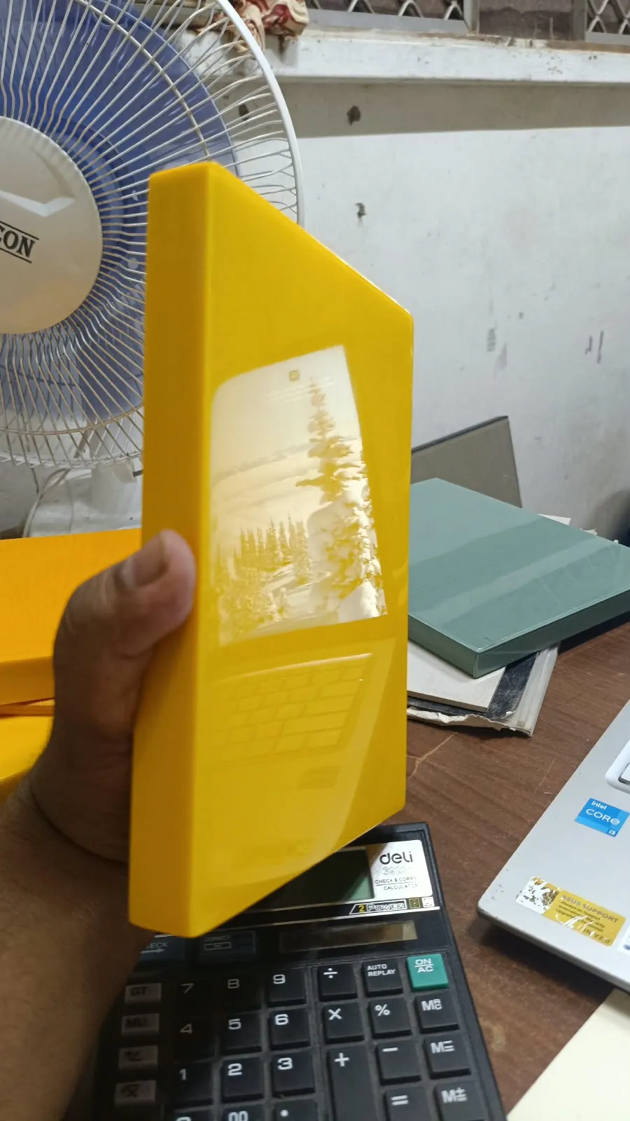 A hand holding a yellow Sunshine Frame sample that reflects a laptop screen